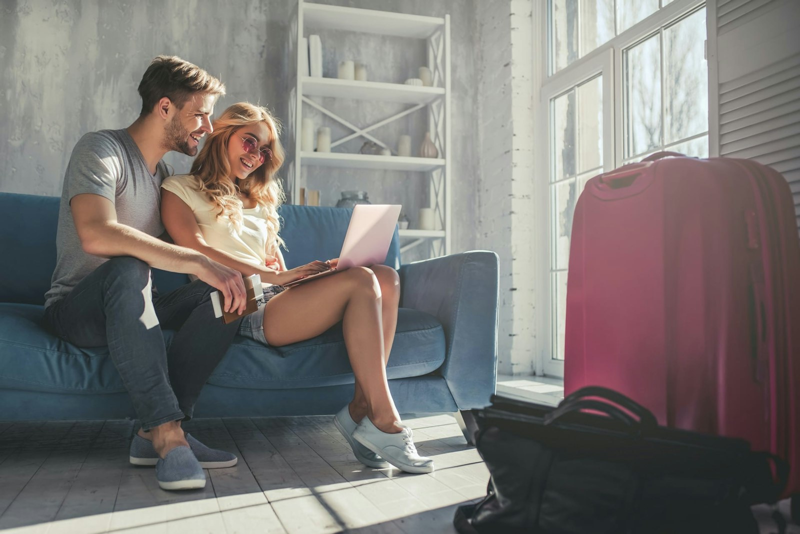 couple Junges Paar sitzt auf dem Sofa einer Ferienwohnung und schaut auf ihren Laptop.