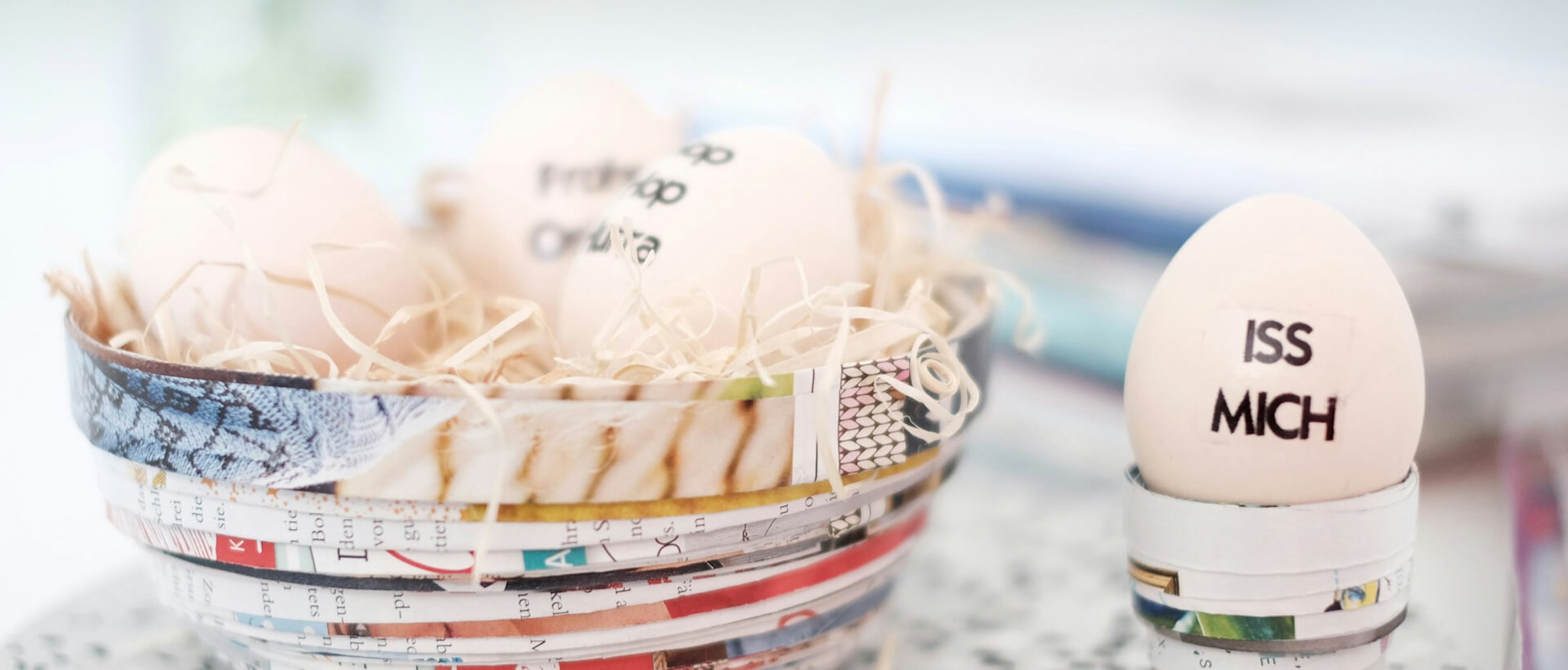 Osternest Das Bild zeigt ein mit drei Eiern gefülltes Osternest aus gefaltetem und zusammengerolltem Zeitschriftenpapier sowie einen Eierbecher aus dem gleichen Material, in dem ein Ei steckt.