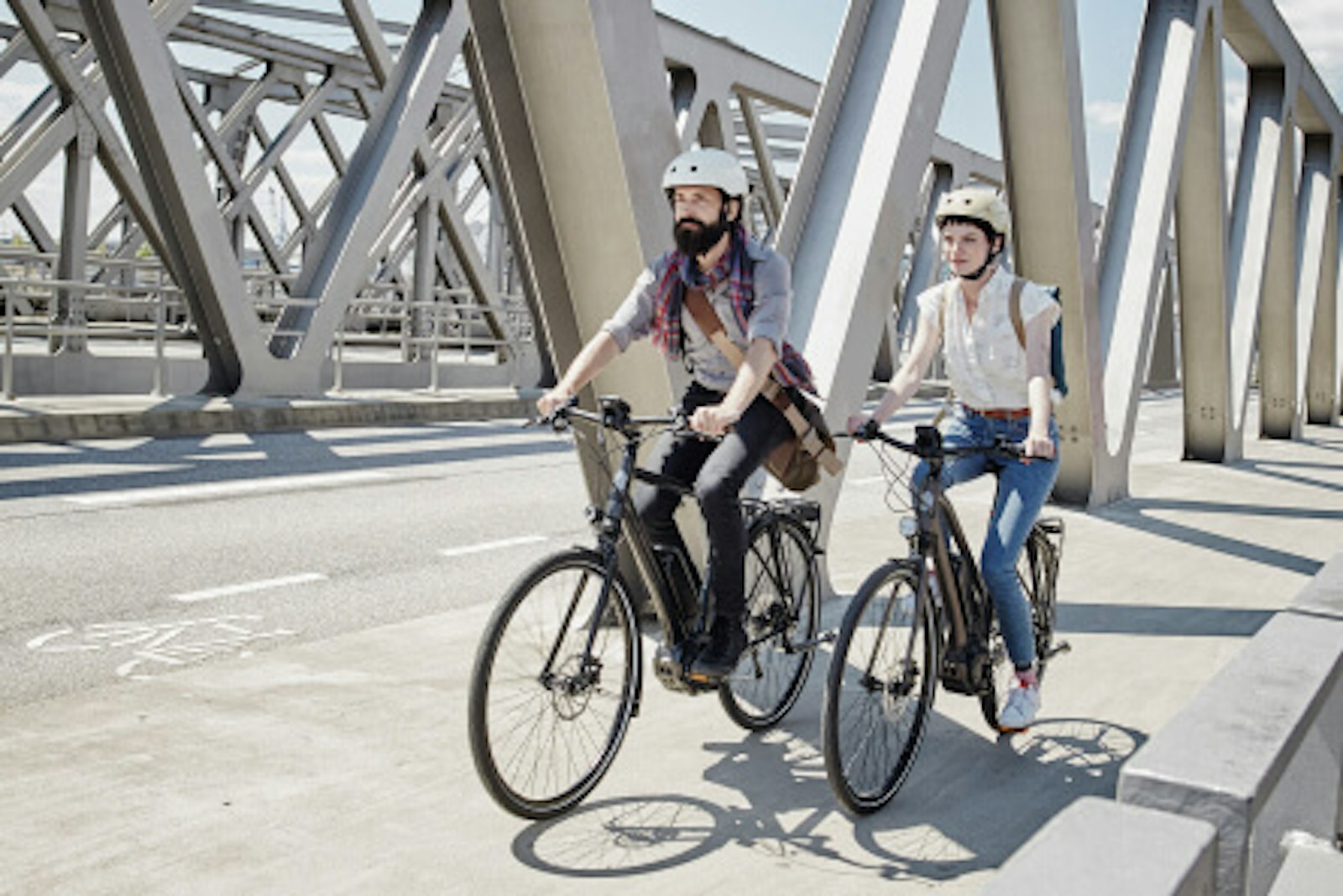 e-bikes-pedelecs-unterschied-fahrradfahrer-bruecke.jpg Das Bild zeigt ein junges Paar, das mit Pedelecs über eine Brücke in einer urbanen Umgebung fährt.