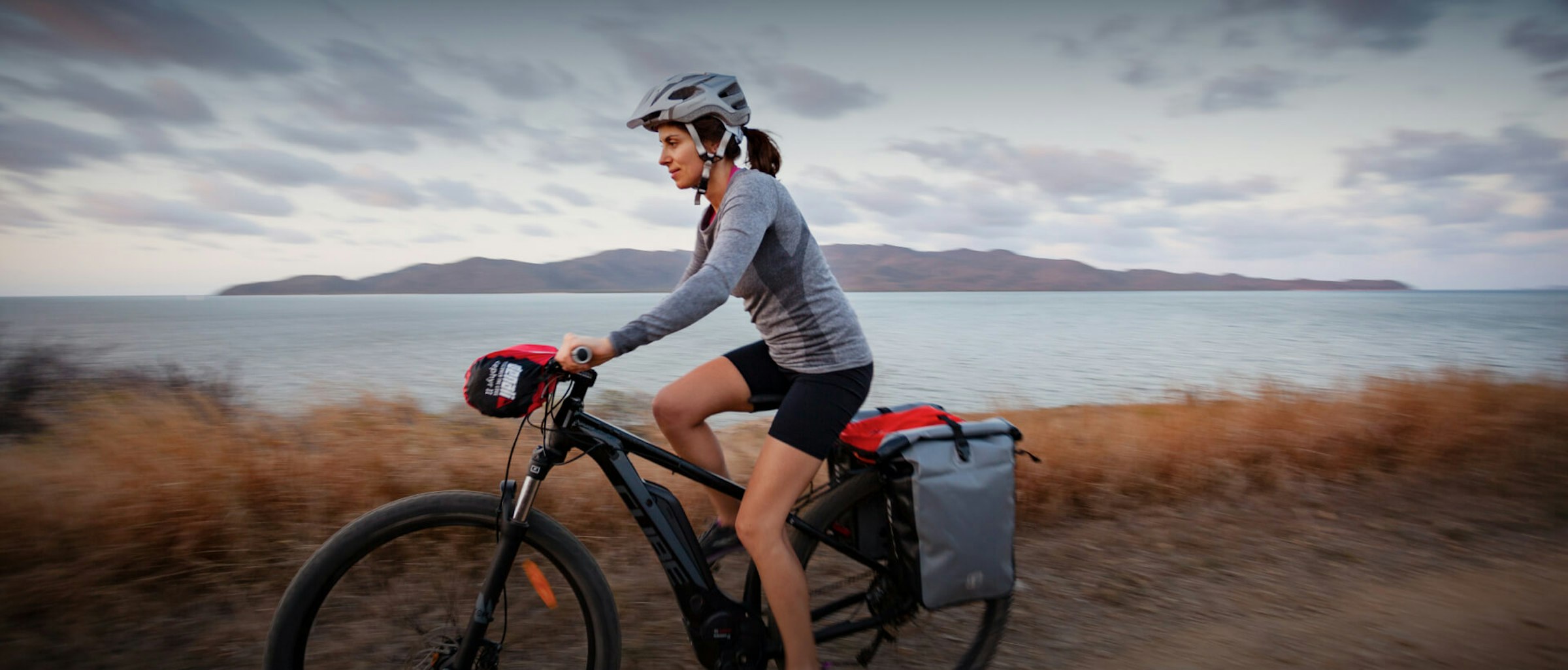 Unterschiede zwischen E-Bike, Pedelec und S-Pedelec Unterschiede zwischen E-Bike, Pedelec und S-Pedelec: Das Bild zeigt eine Frau, die mit ihrem E-Bike entlang einer Küste fährt.