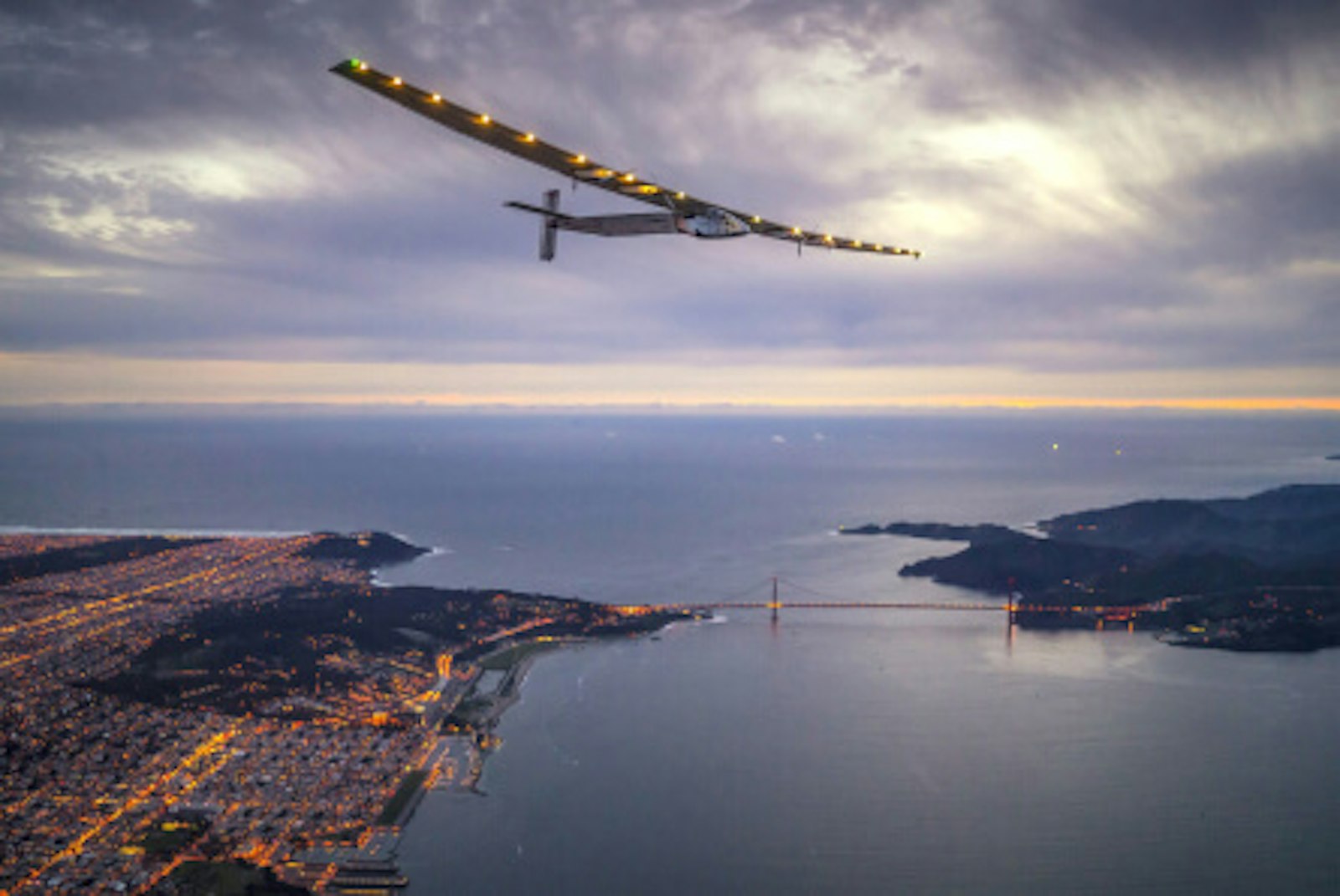 10-fakten-solarenergie-solar-impulse-2.jpg Solarenergie-Fakten: Einsamer Rekord - Alleinflug im Solarflieger. Das Bild zeigt den Solar Impulse 2 fliegend über einer Küste bei Dämmerung.