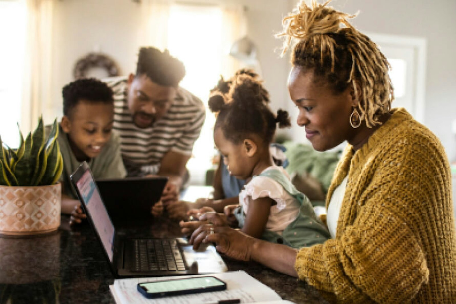 enercity_pe_202_01 Mehrere Mitglieder einer Familie beugen sich nebeneinander sitzend über ihre Tablets, Handys und Laptops.