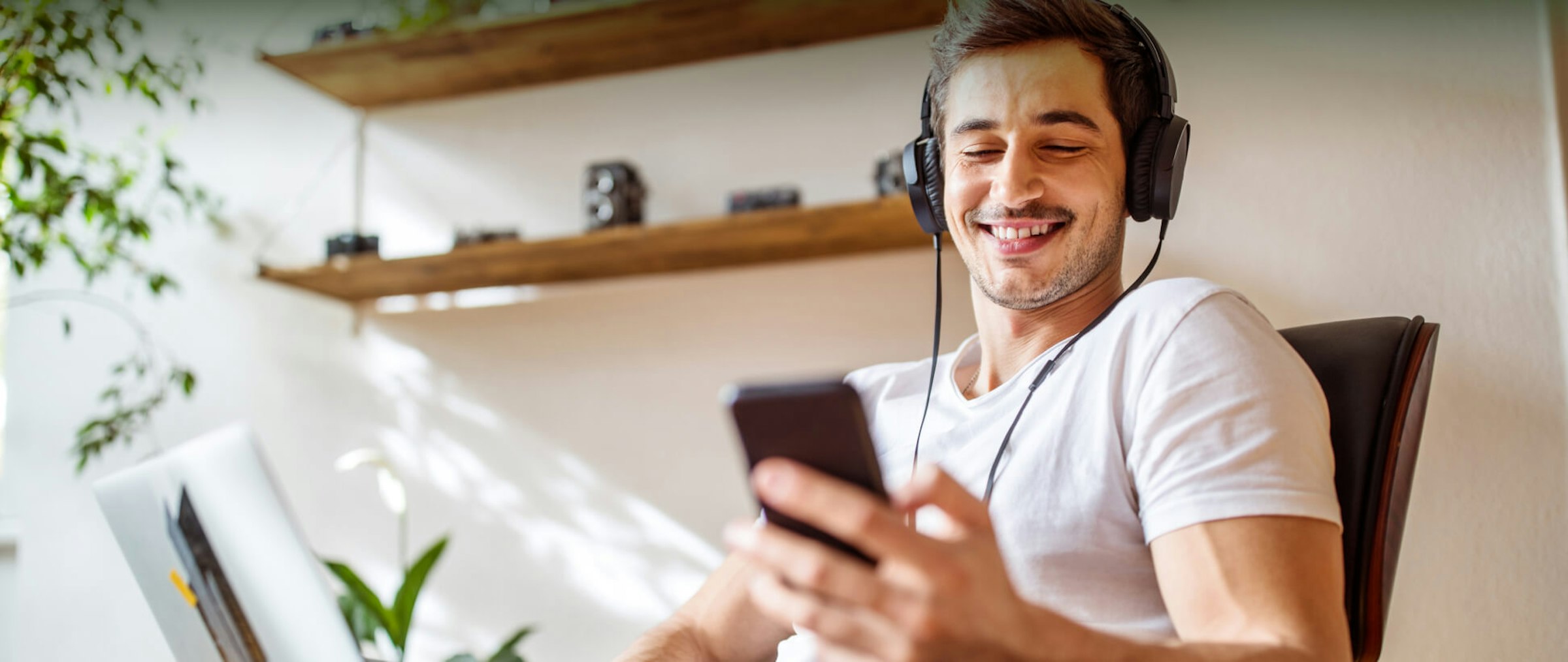 Junger Mann mit Kopfhörern schaut auf sein Handy