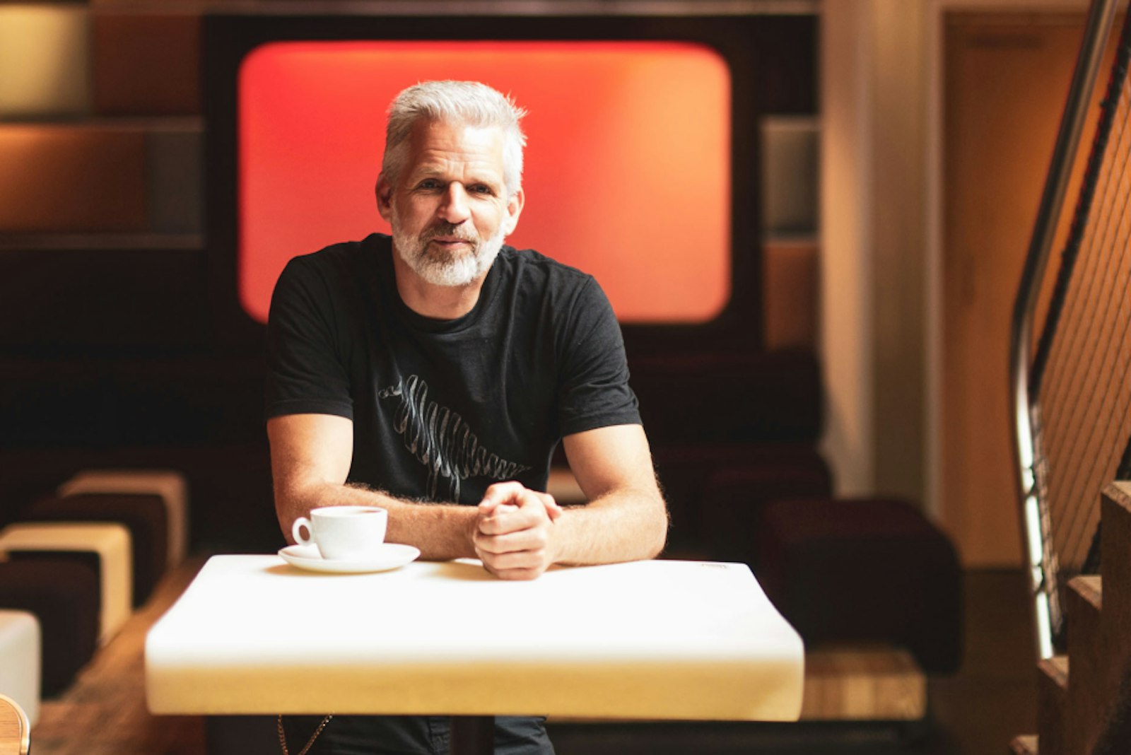 Heiko Heybey Photovoltaik Gastronomie Erfahrung mit Photovoltaik. Dieses Bild zeigt einen Mann, der an einem Tisch sitzt, auf dem eine Tasse steht. Seine Hände hat er ineinander gefaltet.