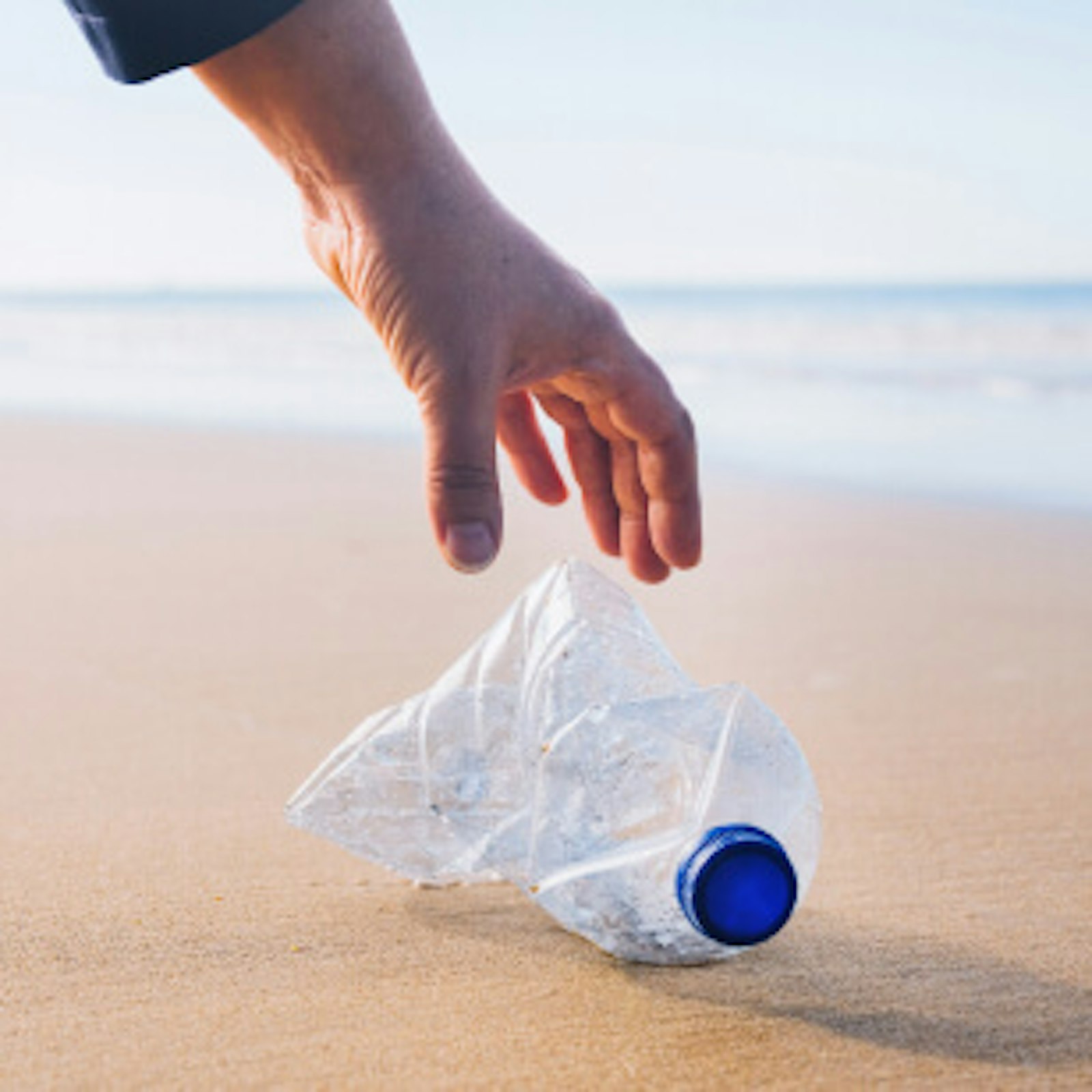 verhalten-am-urlaubsort-nachhaltig-urlaub-machen Hand hebt Plastikflasche auf