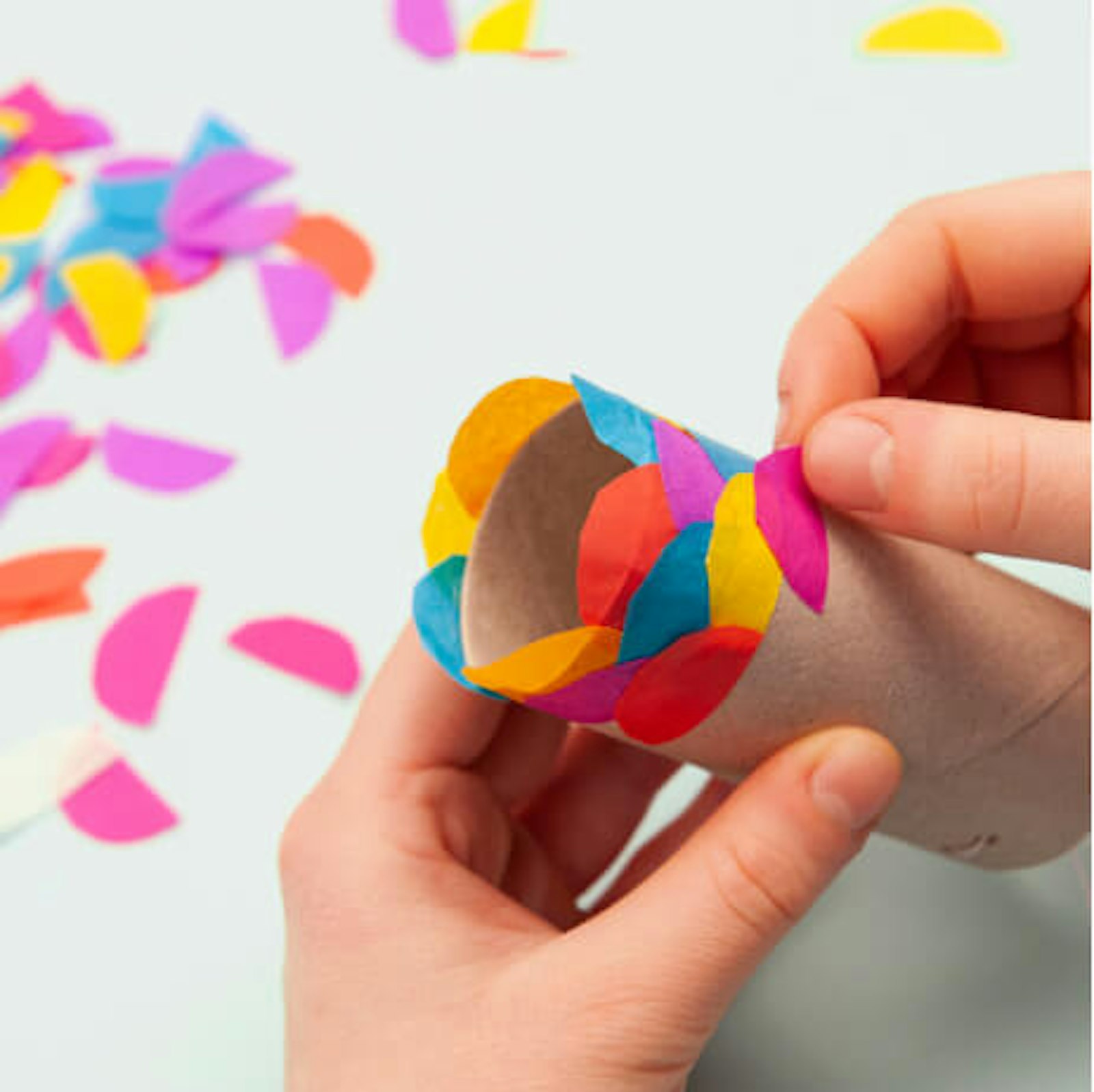 04-fliegende-fische Kinderhände kleben Halbkreise aus Seidenpapier auf eine Klopapierrolle