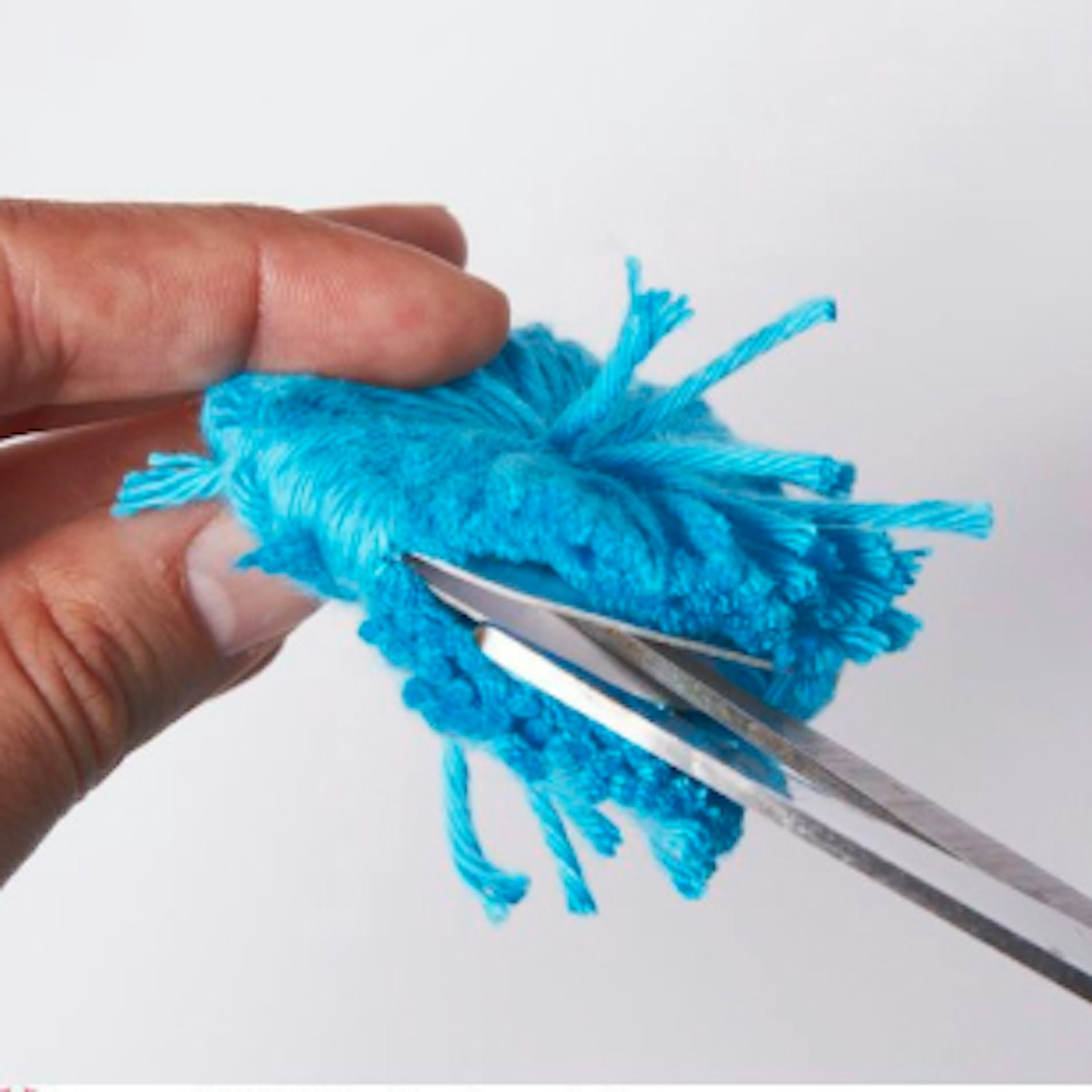 diy-pompons-selber-basteln-schritt-3.jpg Schritt 3: Das Bild zeigt, wie ein Pompon-Rohling mit einer Schere zugeschnitten wird.