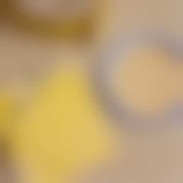 Mit einer Schere wird entlang einer Schablone aus doppelseitigem Klebeband ein Kreis aus einem Stück einer alten Strandmatte geschnitten daneben liegt ein Marmeladenglasdeckel dessen Innenseite bereits mit demselben Material beklebt ist.